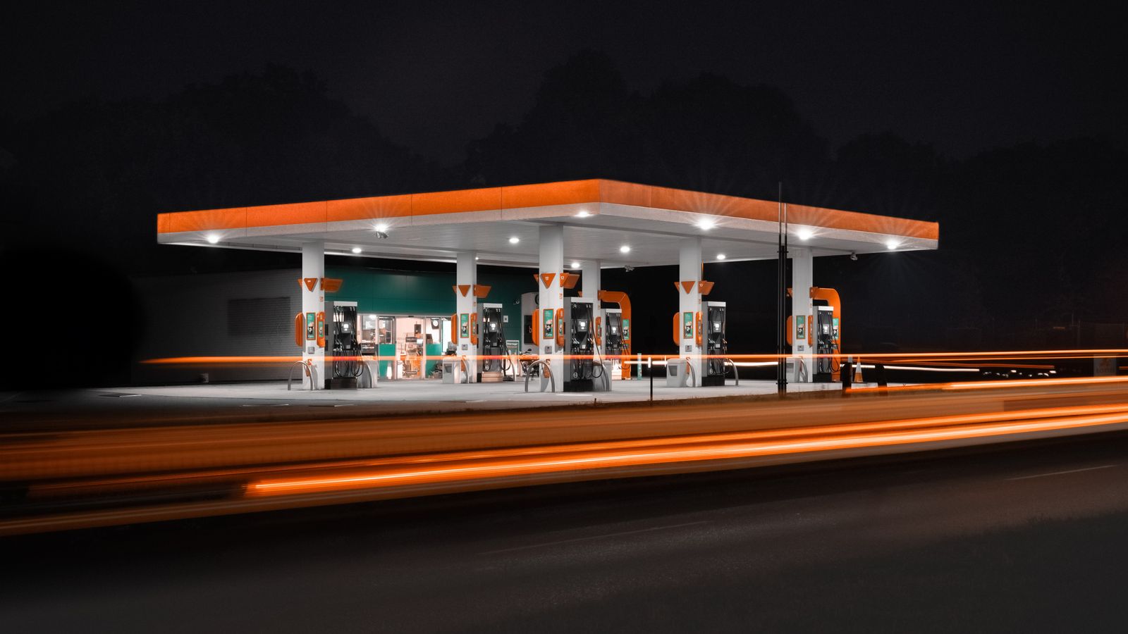 Petrol station lit up at night with traffic light trails