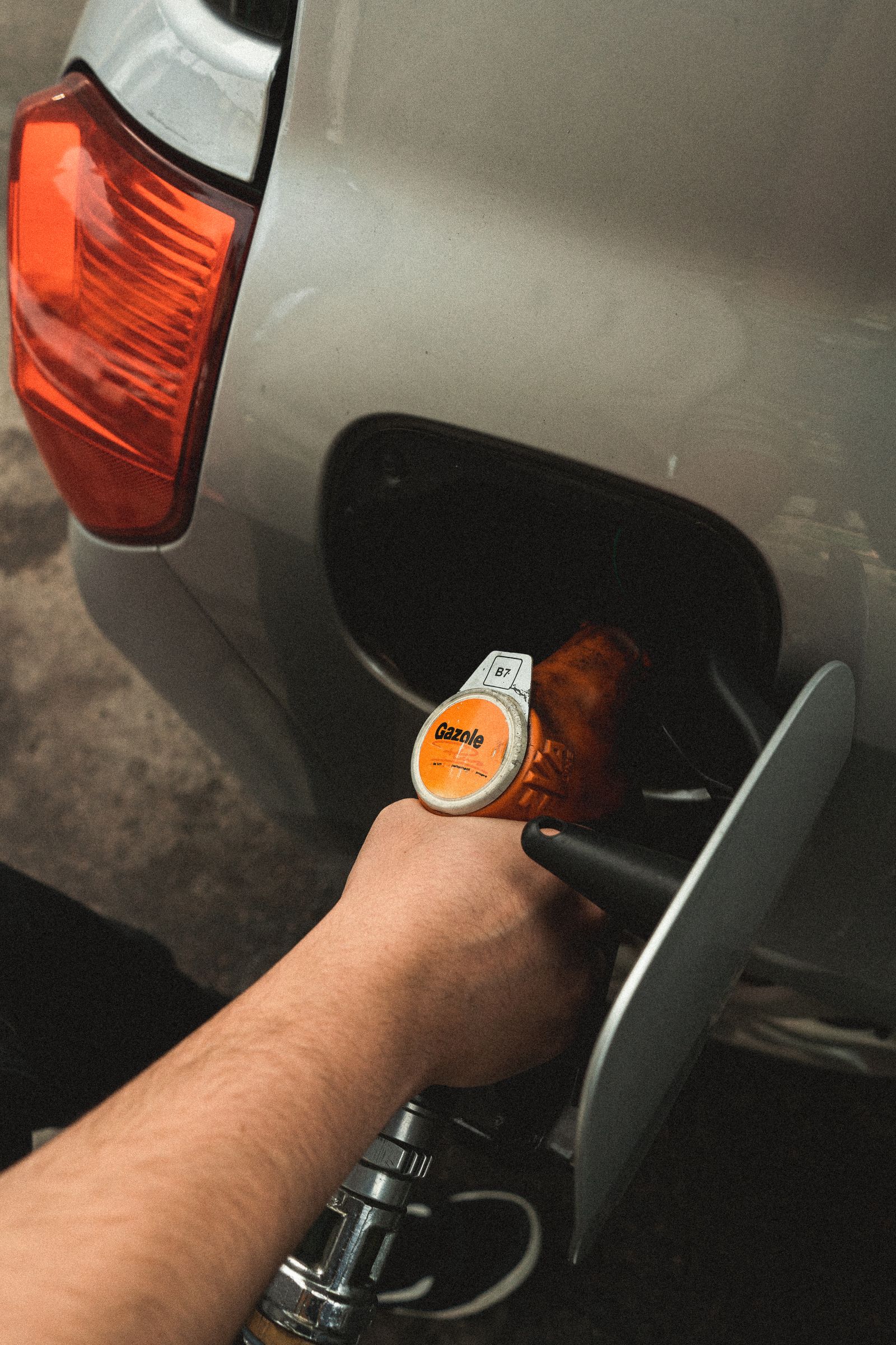 Hand holding a fuel nozzle in an open car fuel filler