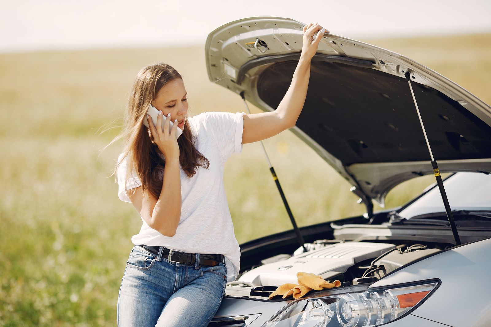 Driver on the phone beside her broken-down car with the bonnet up