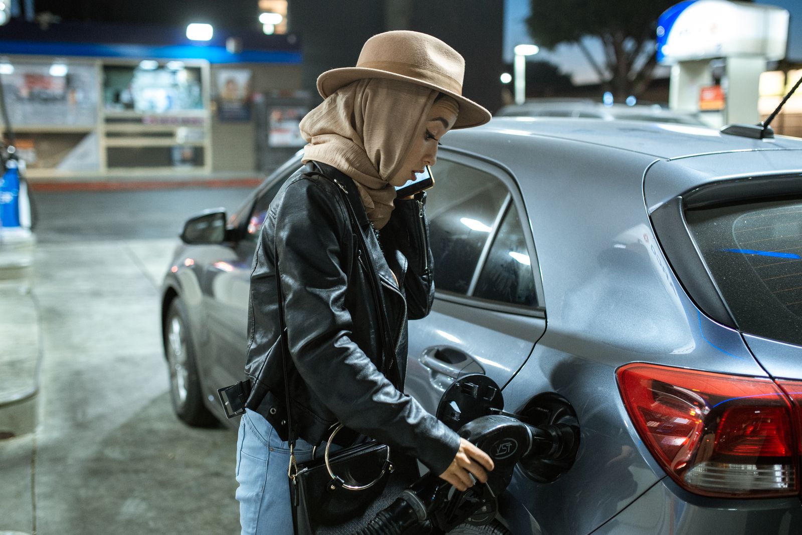 Driver refuelling a hatchback at a petrol station at night