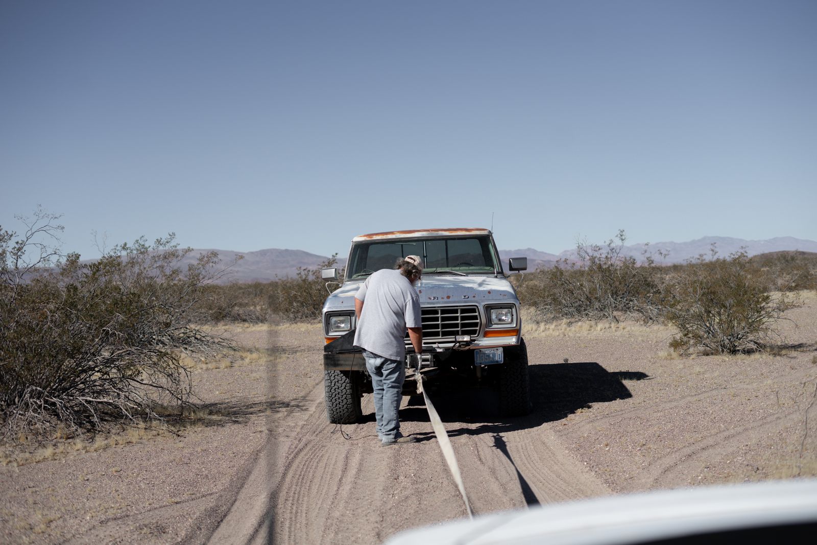Man preparing to tow a broken-down pickup on a desert track